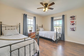 Quarto com duas camas, ventilador de teto e janela com cortinas.