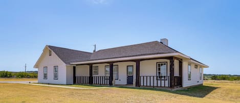 A single-story house with a gabled roof, a front porch with a railing, and a small front yard.