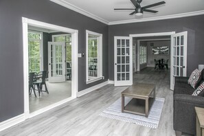 A spacious living room with a grey wall, a ceiling fan, and a dining area with chairs and a table. - Waterfront Deck, Family Arcade! Lake Gaston Home (Bracey)