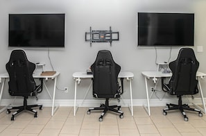 A room with three gaming chairs, two desks, and two large flat-screen TVs mounted on the wall. - Waterfront Deck, Family Arcade! Lake Gaston Home (Bracey)