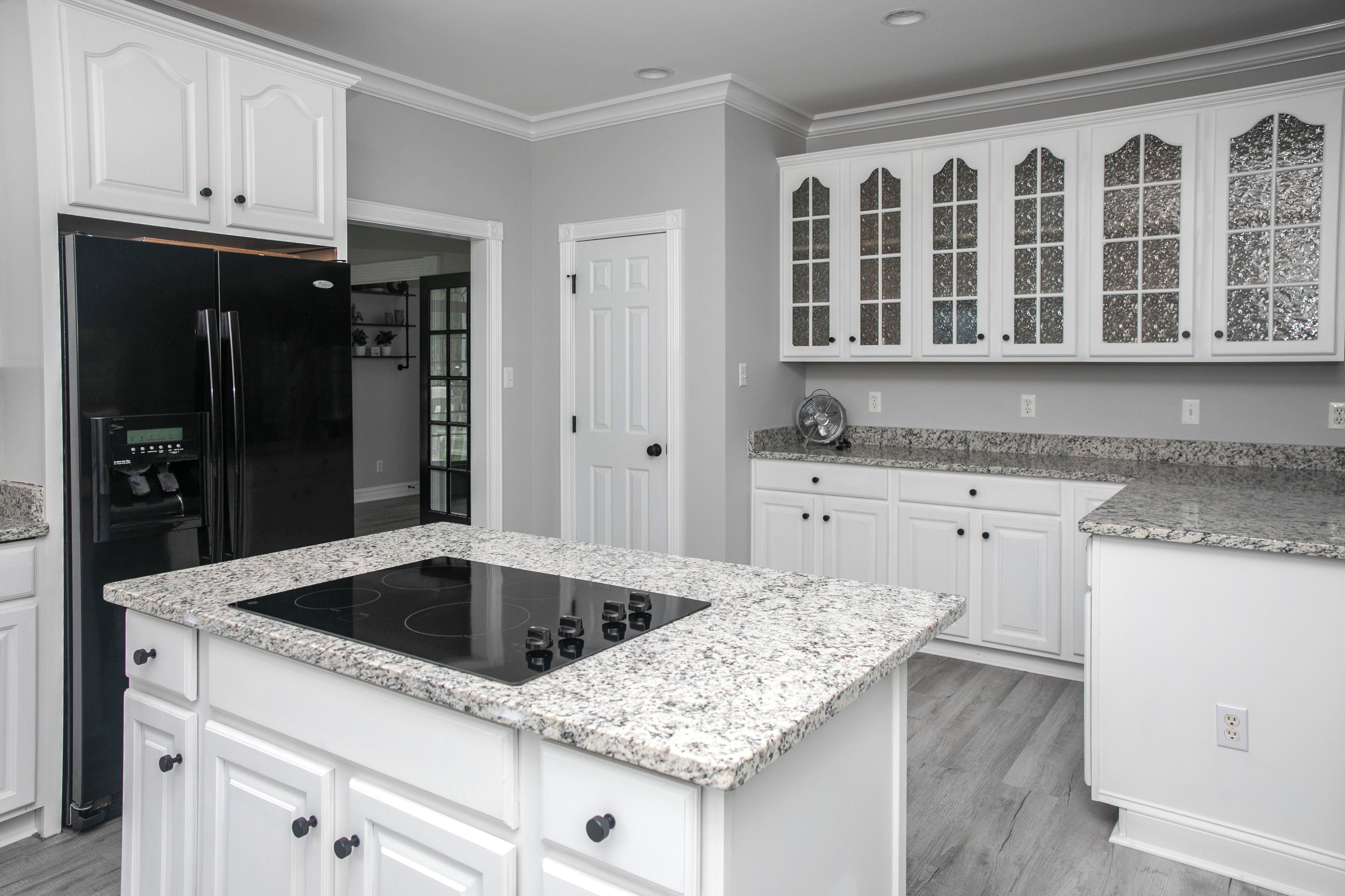 A modern kitchen with white cabinetry, a black refrigerator, and a granite countertop.
