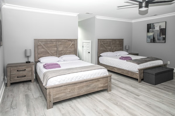 A bedroom with two wooden beds, a nightstand, a bedside table, a floor lamp, and a ceiling fan. - Waterfront Deck, Family Arcade! Lake Gaston Home (Bracey)
