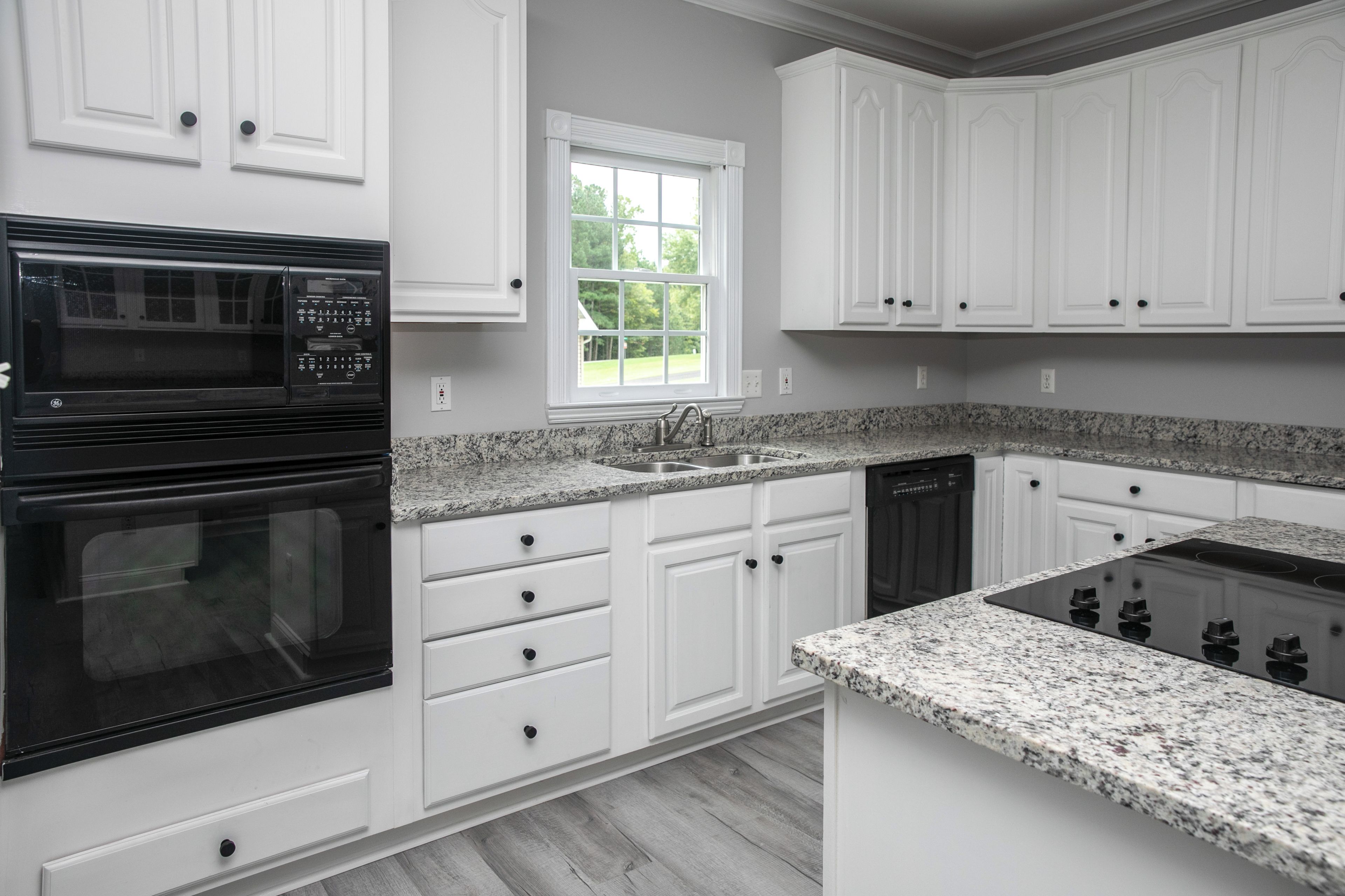 A modern kitchen with white cabinetry, a built-in oven, a dishwasher, and granite countertops.