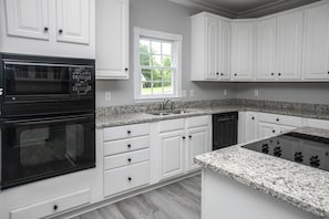 A modern kitchen with white cabinetry, a built-in oven, a dishwasher, and granite countertops. - Waterfront Deck, Family Arcade! Lake Gaston Home (Bracey)