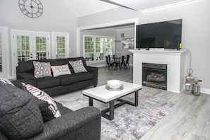 A living room with a sofa, a coffee table, and a fireplace. - Waterfront Deck, Family Arcade! Lake Gaston Home (Bracey)
