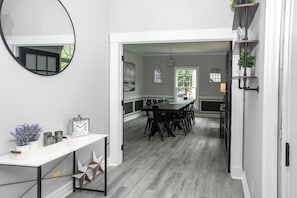Un coin repas avec une table ronde et des chaises, une console blanche agrémentée d’objets décoratifs et un grand miroir au mur.