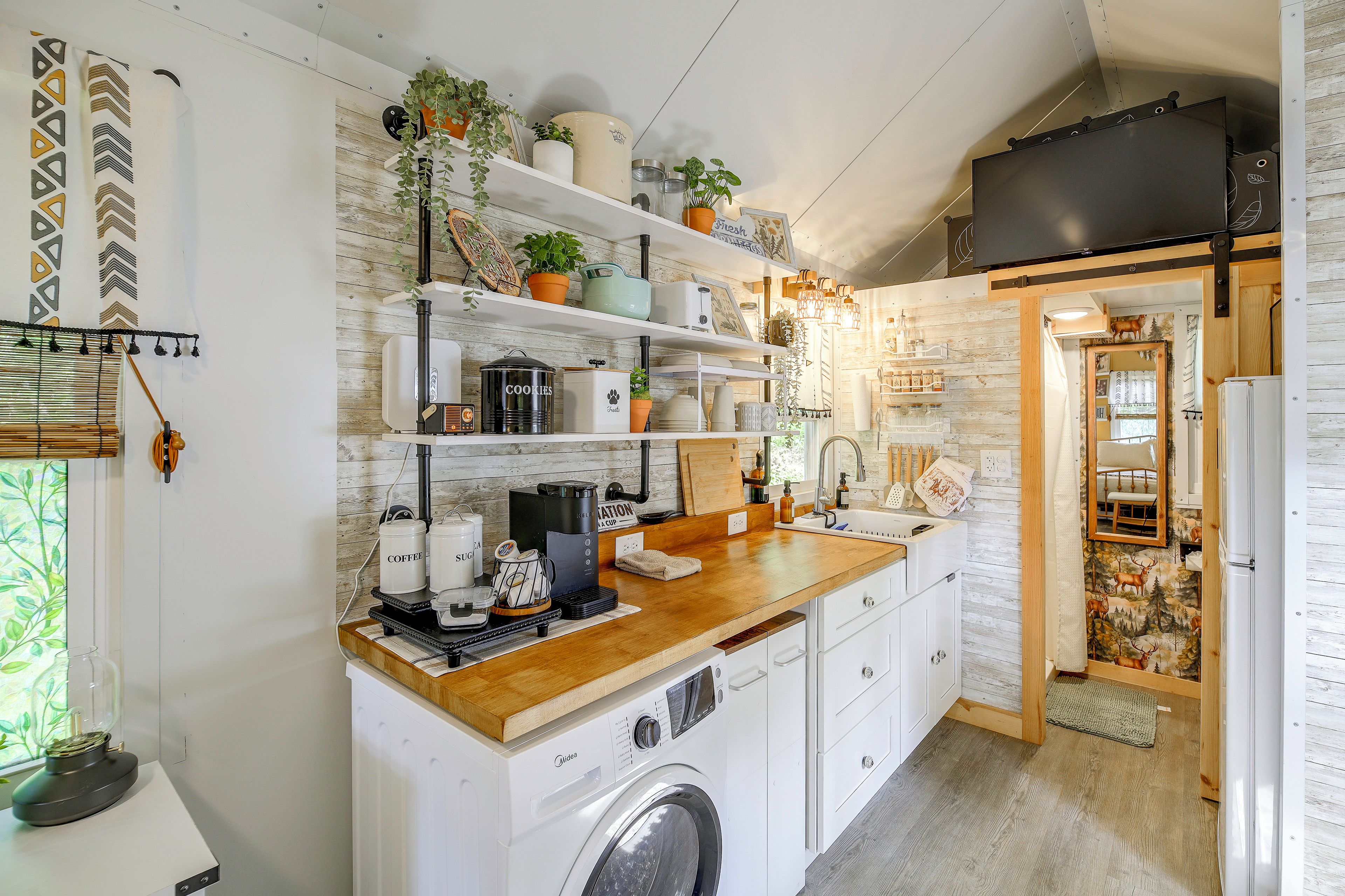 A compact kitchen with a built-in washing machine, a coffee station, and a variety of potted plants.