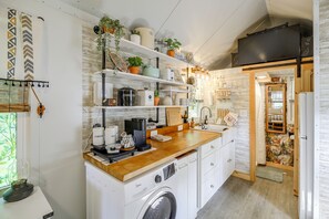 Cocina compacta con lavadora integrada, área de café y varios maceteros.