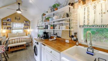 A compact kitchen with a washing machine, a coffee station, and a sink.