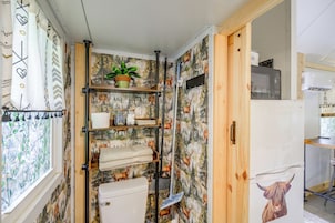 Un baño pequeño con ducha, inodoro y repisas con artículos de aseo.
