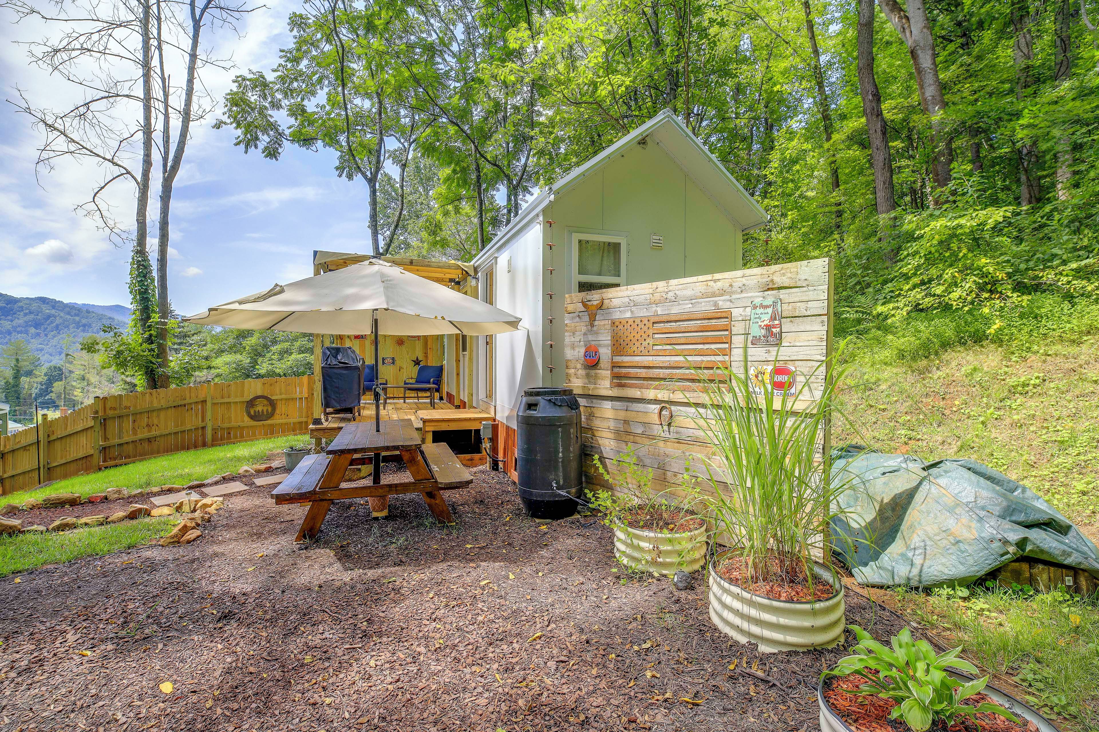 A small cabin with a patio area, a wooden fence, and a view of the surrounding forest.