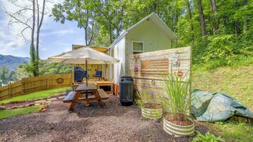 A small cabin with a patio area, a wooden fence, and a view of the surrounding forest.