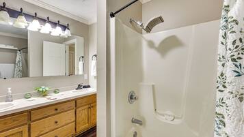 A bathroom with a wooden vanity, a mirror, a shower with a handheld showerhead, and a towel rack.