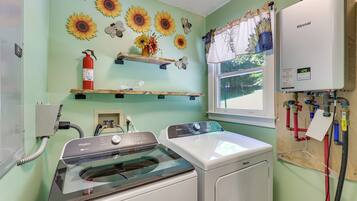 A laundry room with a Whirlpool washer and dryer, a fire extinguisher, and a window with a view of greenery.