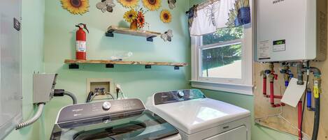 A laundry room with a Whirlpool washer and dryer, a fire extinguisher, and a window with a view of greenery.