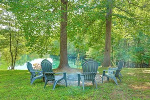 A lakeside seating area with four Adirondack chairs and a small fire pit.