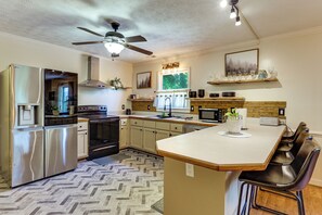 A modern kitchen with stainless steel appliances, a herringbone-patterned floor, and a central island with bar stools.