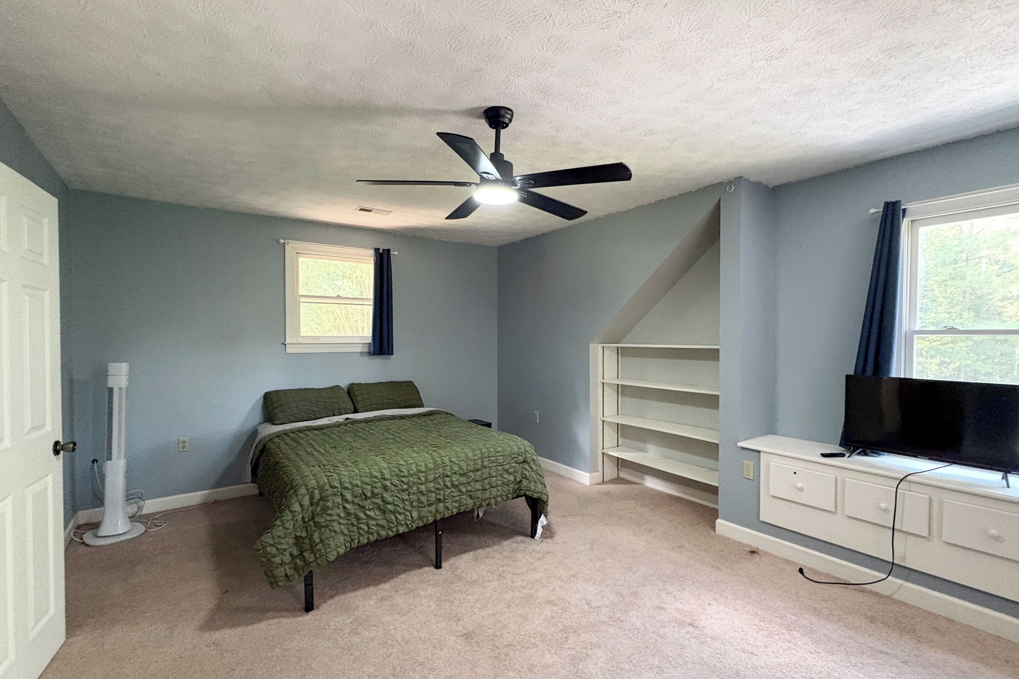 A bedroom with a bed, a ceiling fan, a window, a TV, and a dresser.
