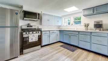 A modern kitchen with a stainless steel refrigerator, a gas stove, a microwave, and light blue cabinets.