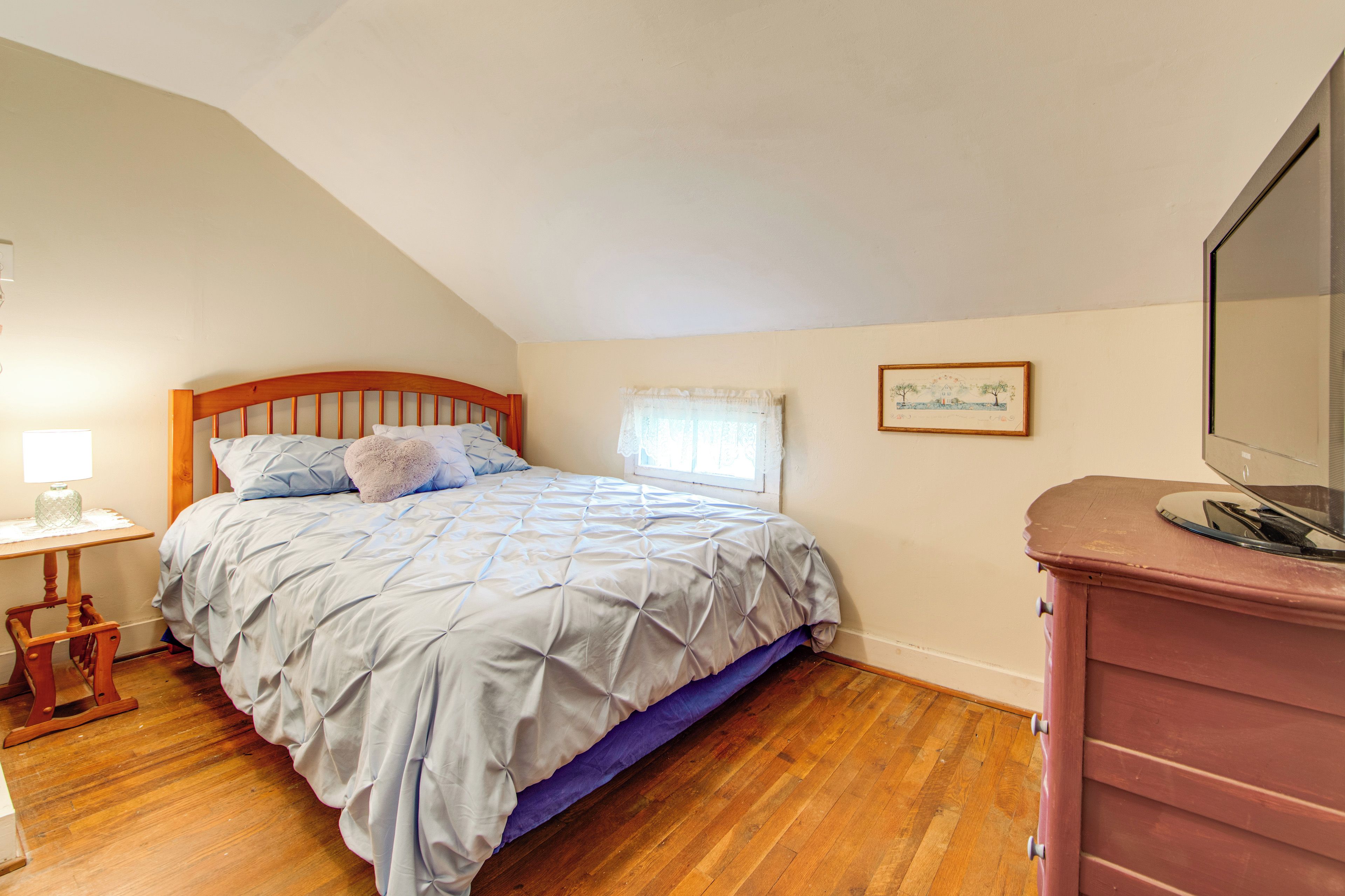 A bedroom with a wooden bed, a nightstand, a dresser, and a window with curtains.