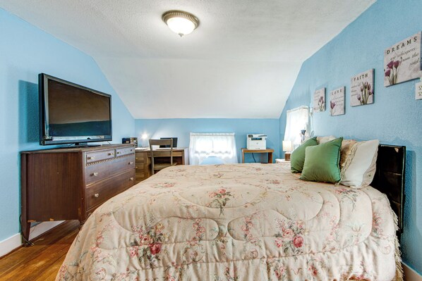 A bedroom with a bed, dresser, television, desk, and wall decorations.