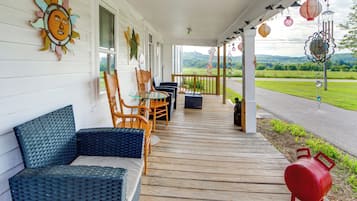 A covered porch with wicker furniture, a barbecue grill, and decorative elements like a sun decoration and hanging lanterns.