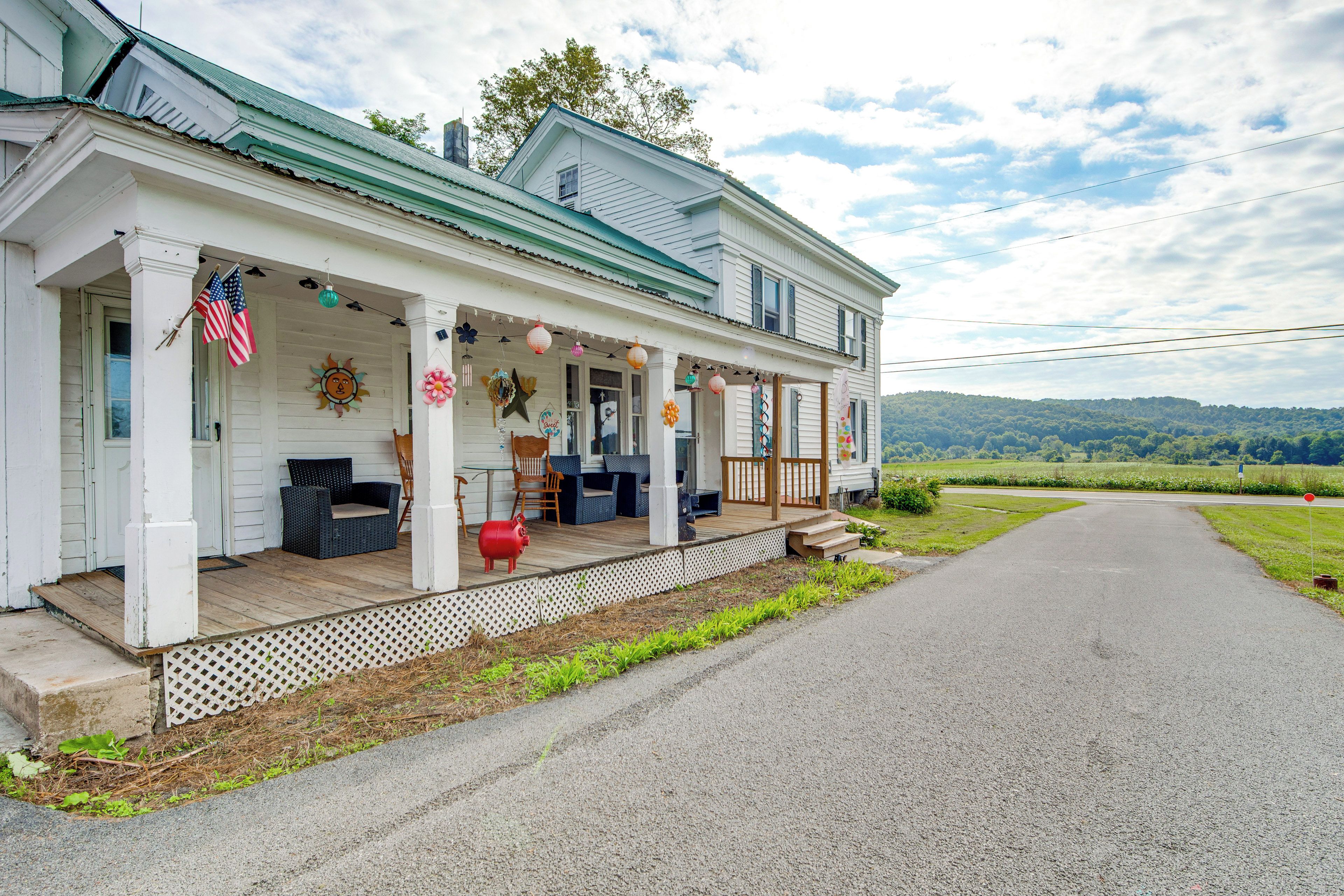 A two-story house with a porch, outdoor seating, and a view of the countryside.