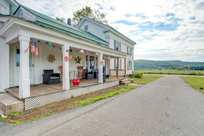 A two-story house with a porch, outdoor seating, and a view of the countryside.