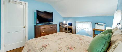Une chambre à coucher comprenant un lit, une commode, une télévision, un bureau et une fenêtre avec des rideaux.