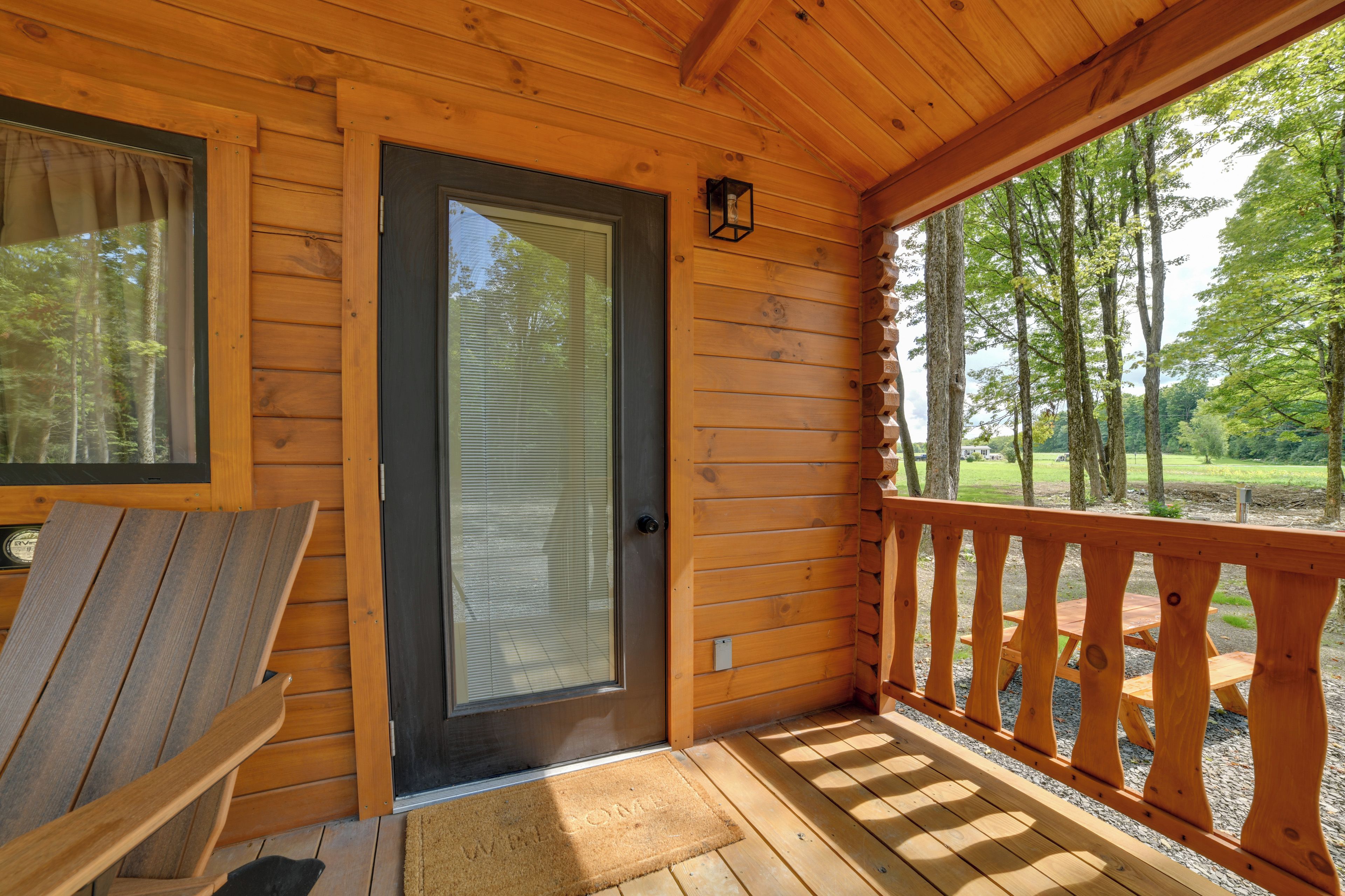 A wooden cabin with a sliding glass door, a deck with wooden railings, and a view of a forest.