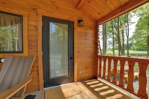 A wooden cabin with a sliding glass door, a deck with wooden railings, and a view of a forest.