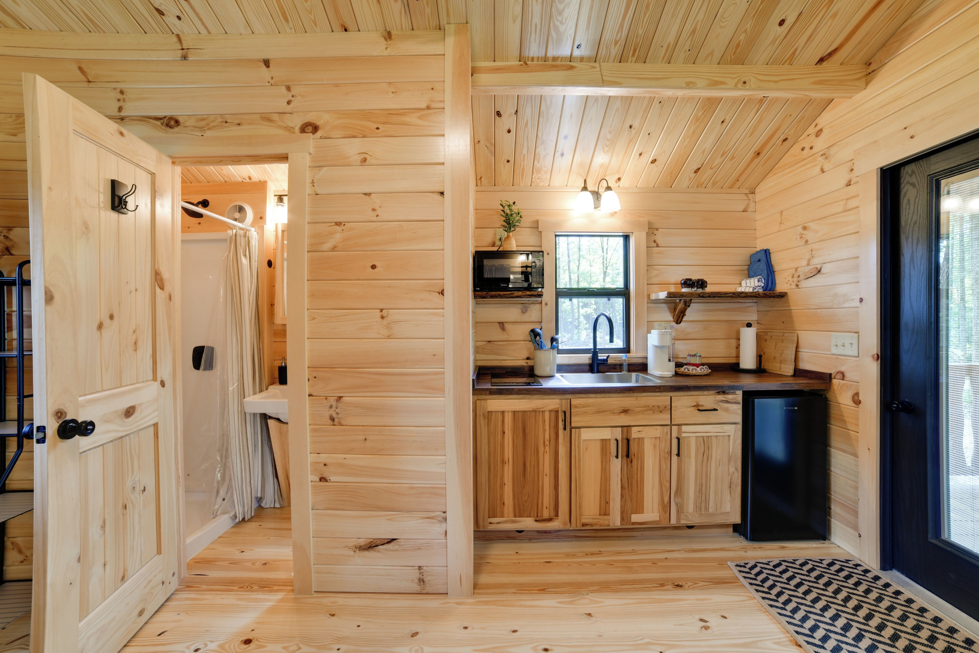 A wooden interior with a kitchen area featuring a sink, cabinets, and a refrigerator.