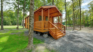 A wooden cabin with a porch and steps, surrounded by trees and gravel ground.
