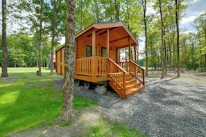 A wooden cabin with a porch and steps, surrounded by trees and gravel ground.