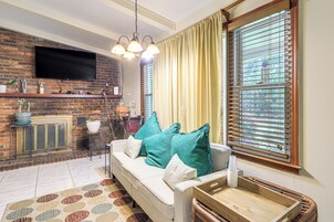 Una sala de estar con chimenea de ladrillo, un sofá con cojines color turquesa y un amplio ventanal con persianas.