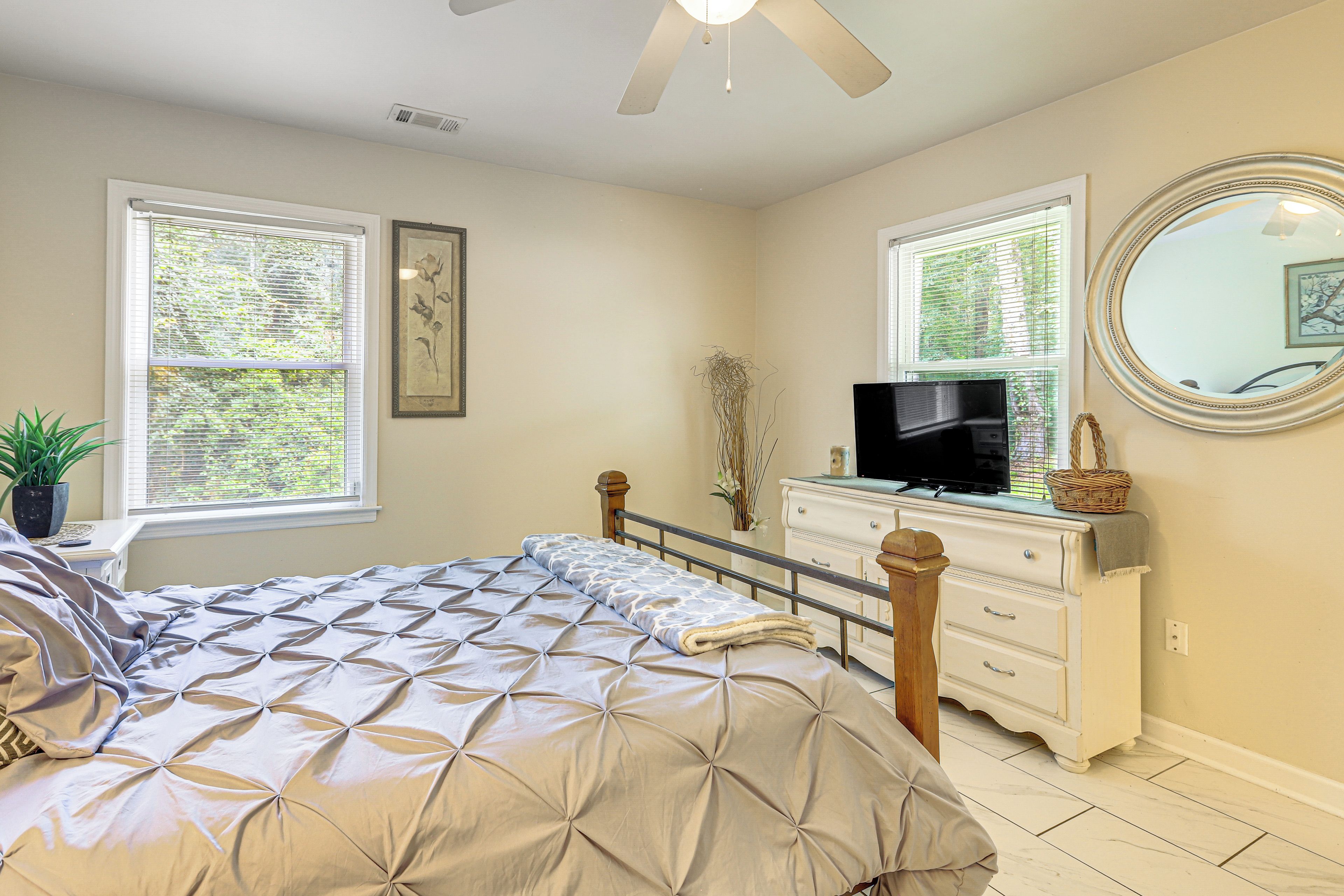 Quarto com cama, cômoda, televisão, janelas e ventilador de teto.