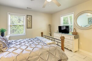 Un dormitorio con cama, cómoda, televisor, ventanas y ventilador de techo.