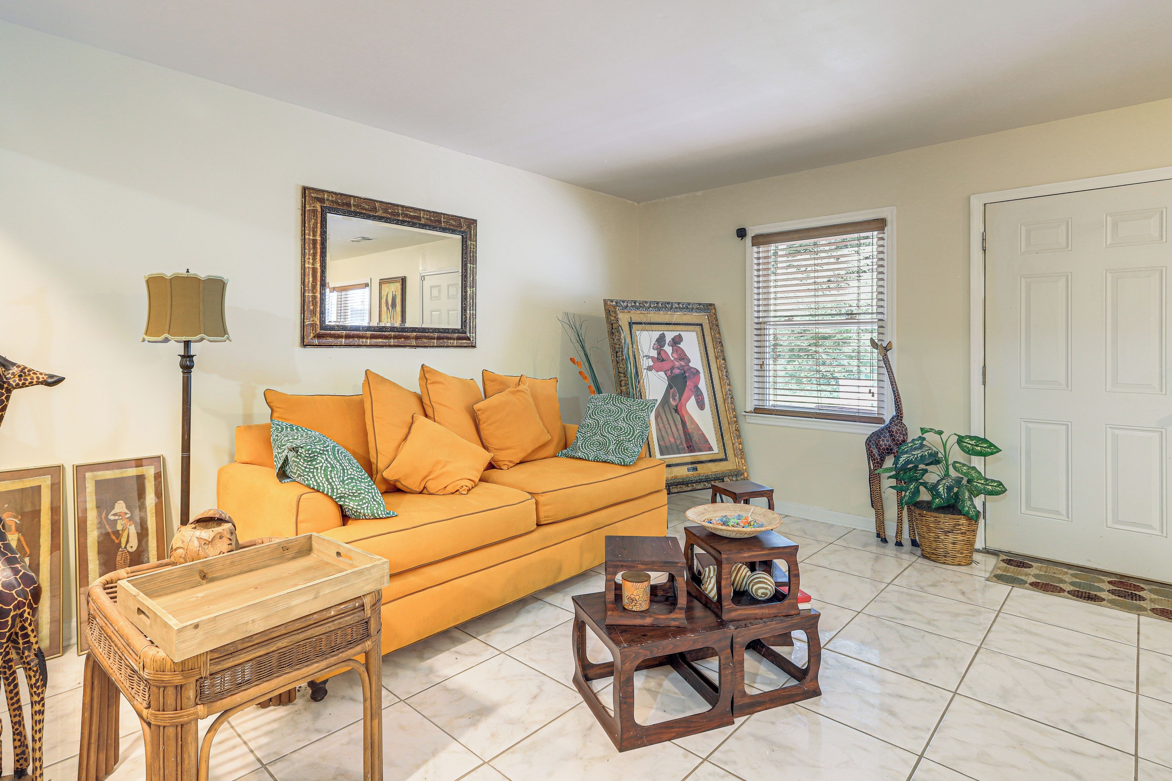A living room with a sofa, a coffee table, a lamp, a framed mirror, and a giraffe statue.