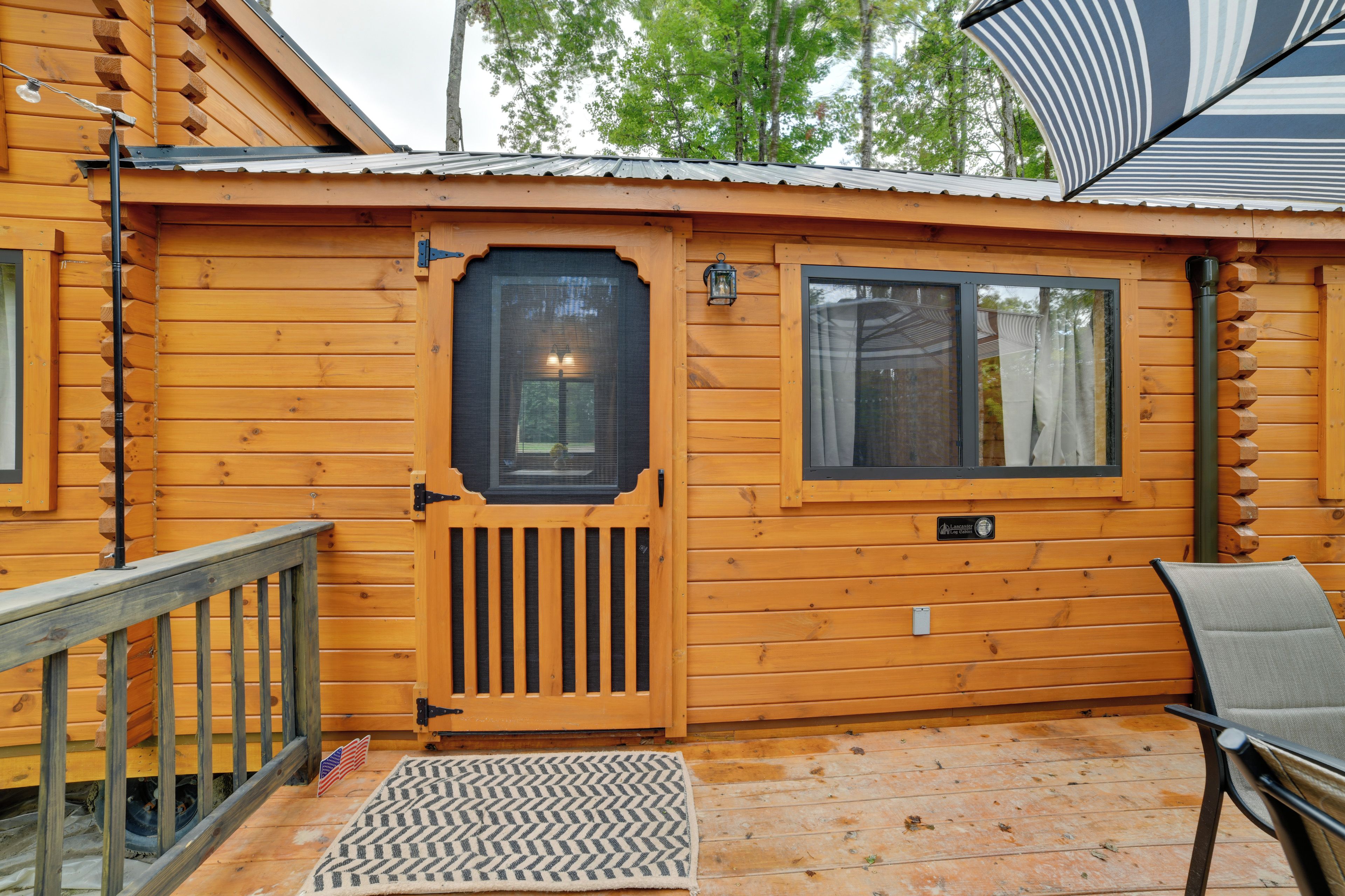 A wooden cabin with a front door, a window, a porch with a chair, and a small American flag.