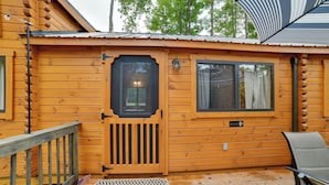 En stuga av trä med en ytterdörr, ett fönster, en veranda med en stol och en liten amerikansk flagga.