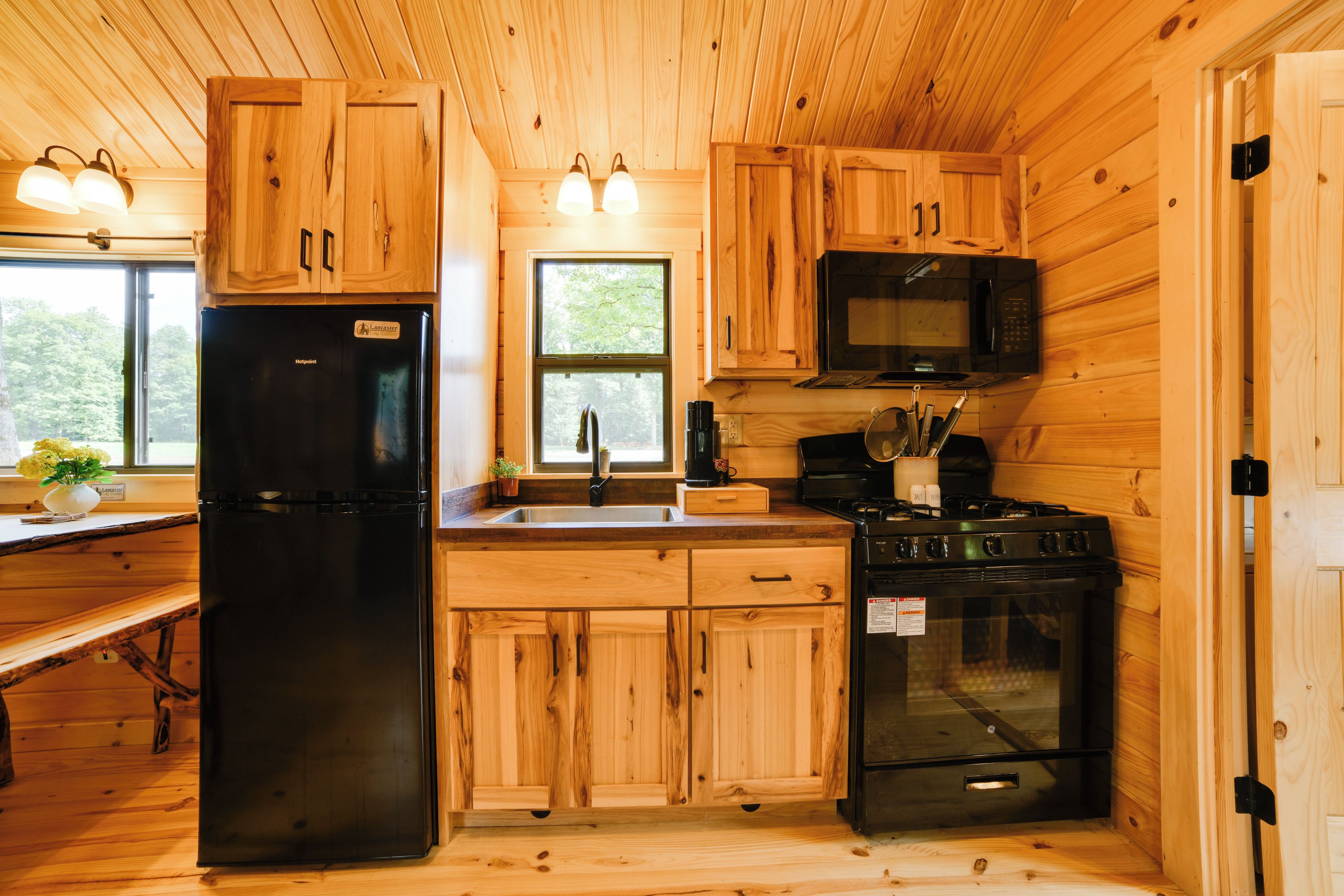 A compact kitchen with wooden cabinetry, a refrigerator, a microwave, and a stove.