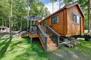 A wooden cabin with a deck and stairs, surrounded by trees.