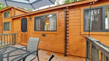 A wooden cabin with a deck, a table with chairs, and a window with curtains.