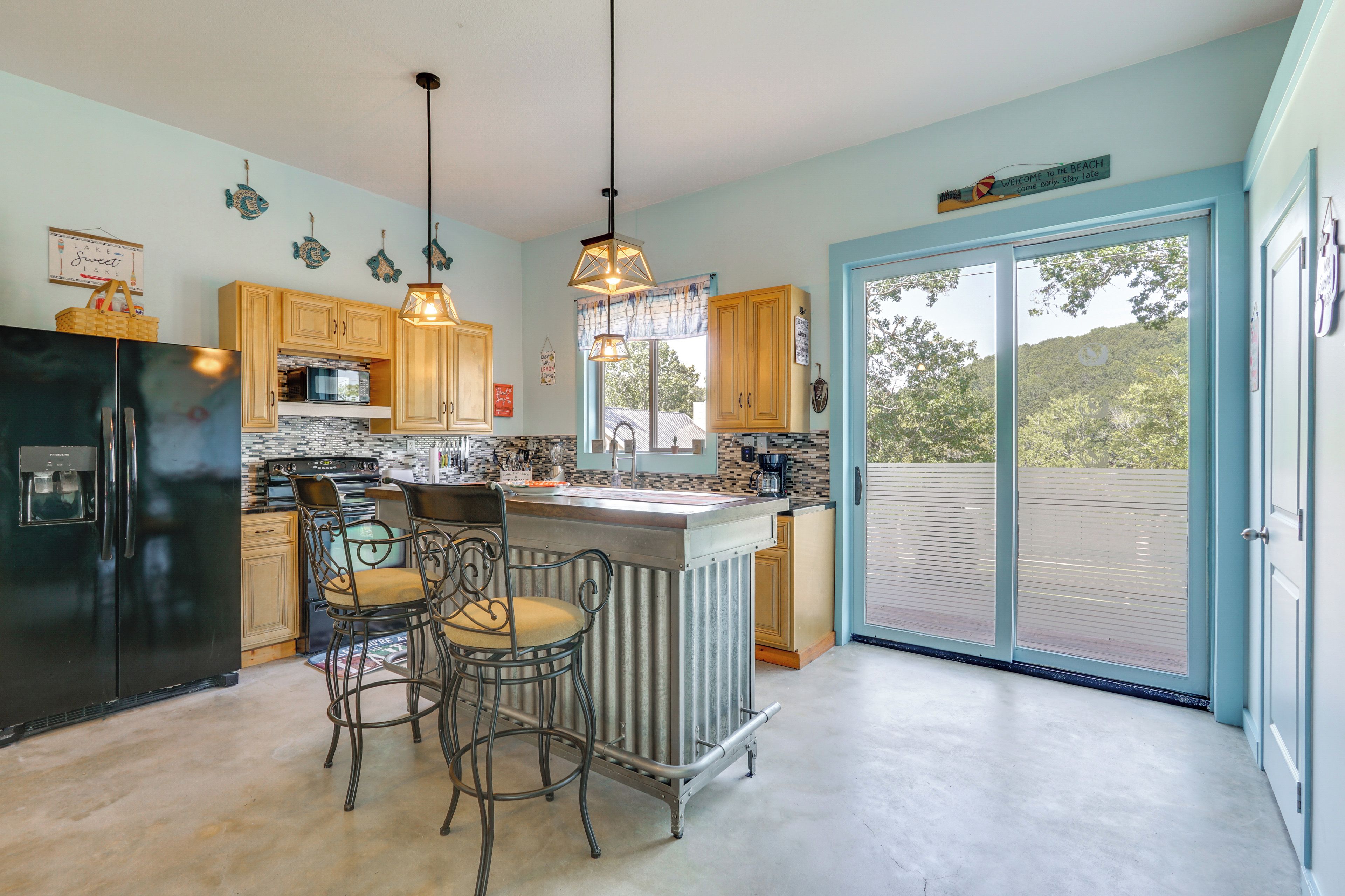 A kitchen with a refrigerator, stove, and bar area with chairs.