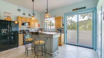 A kitchen with a refrigerator, stove, and bar area with chairs.