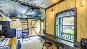 A rustic interior with a bunk bed, a bar area with stools, a ladder, and a large window. - Near ATV Trails! Coal Heritage Cabin w/ Fire Pit (Roderfield)