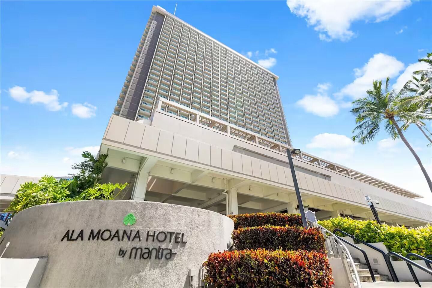 A hotel building with a modern design, a sign indicating it's the Ala Moana Hotel by Mantra, and a clear sky in the background.