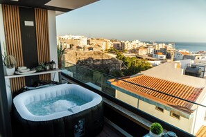 Un balcon avec un jacuzzi, une vue sur le paysage urbain et une plante en pot.