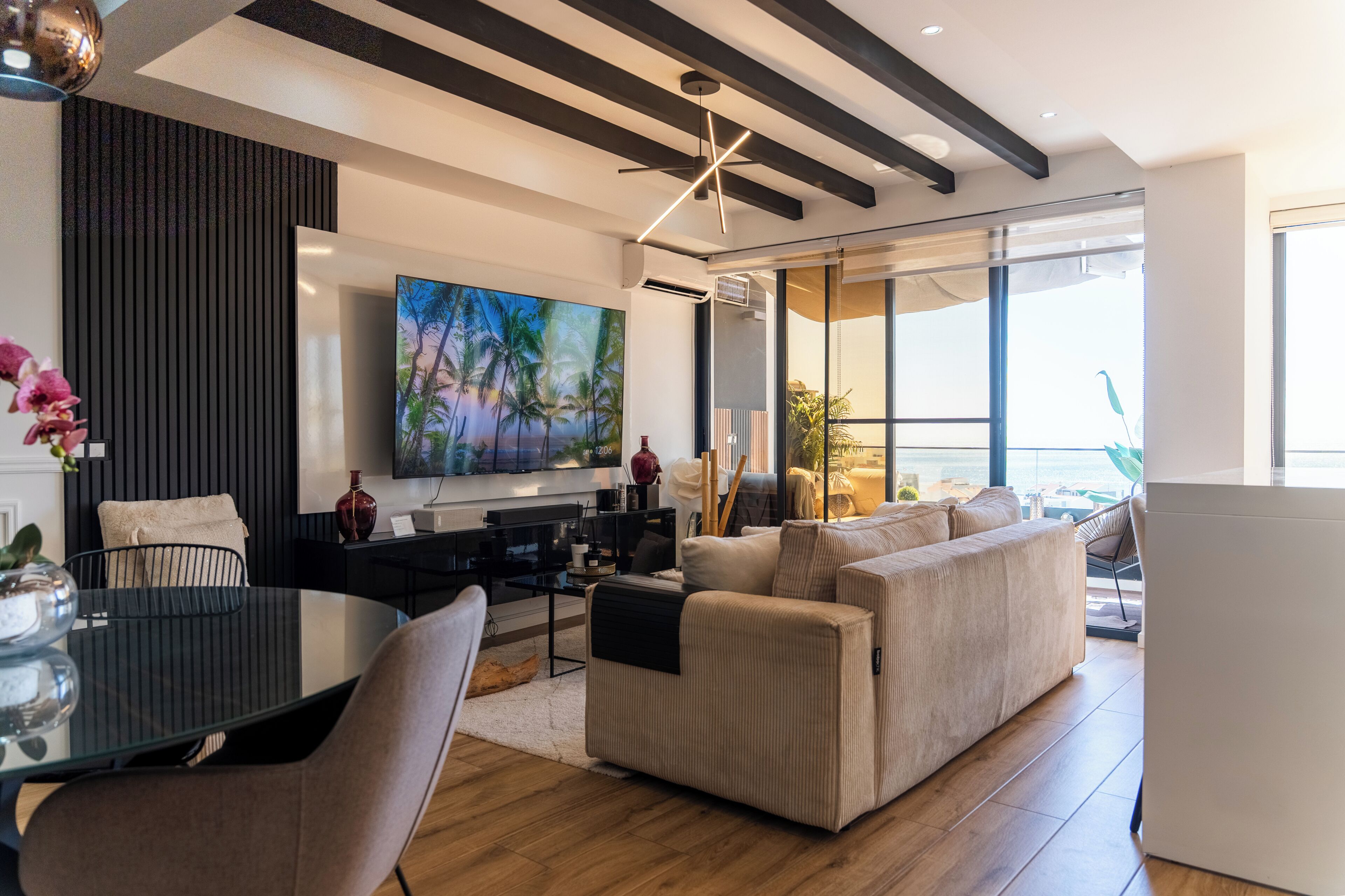 Una sala de estar moderna con un televisor de pantalla plana grande, un sofá, una mesa de comedor con sillas y un jarrón decorativo.