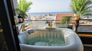 Ett bubbelbad på en balkong med utsikt över havet och byggnaderna.